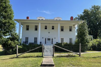 White two-story historic house behind a wire fence.